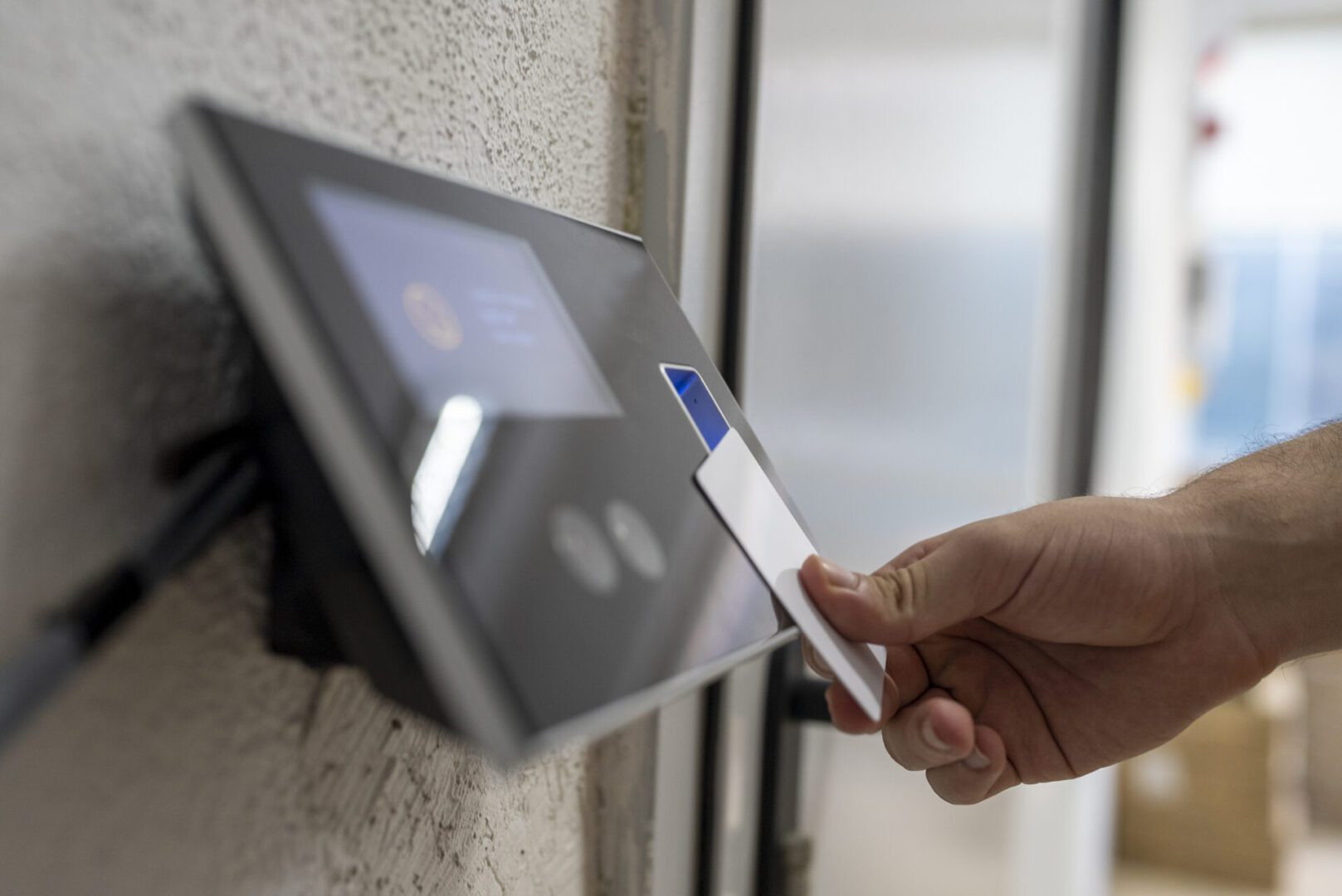 A person holds an access card up to an electronic card reader mounted on a wall.