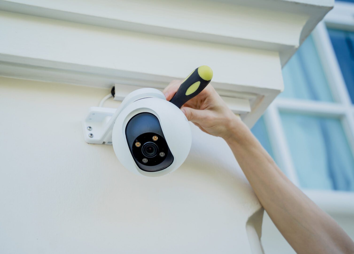 A person installs or adjusts an outdoor security camera on a building exterior using a screwdriver.