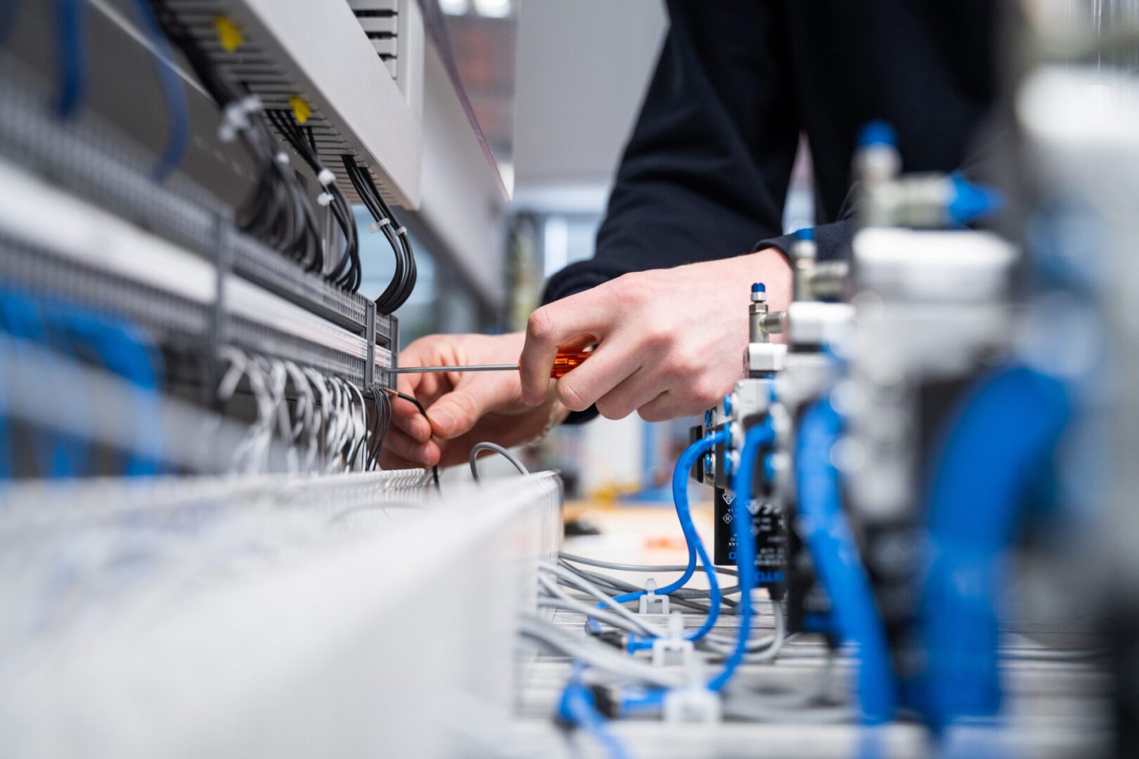 Person connecting wires and using a screwdriver on an industrial control panel with various cables and blue components.