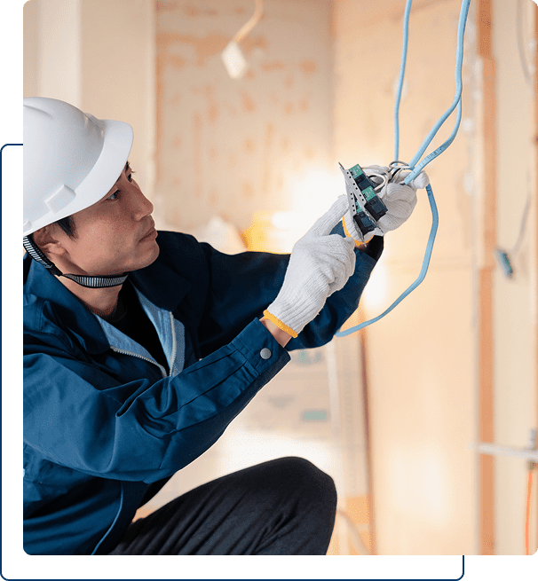 A person wearing a white hard hat and gloves installs or repairs electrical wiring inside a building under construction.